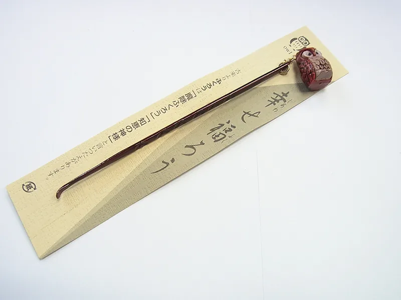木目調の細長い台紙に付いた1点。先の曲がった細い棒の上端に、赤茶色のふくろうの飾りが付いている
