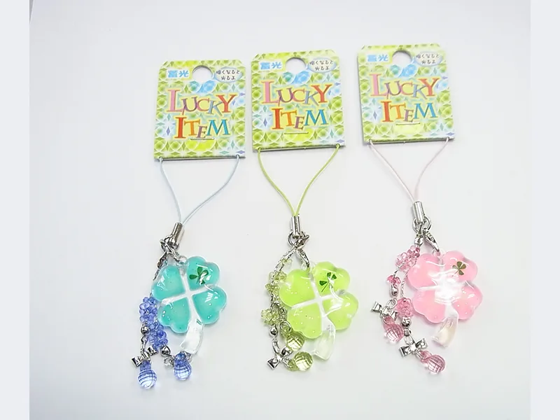 「LUCKY ITEM」の台紙に付いた、クローバー形のストラップ3色。水色・黄緑・ピンク。同じ色の小さな玉が房のように下がっている