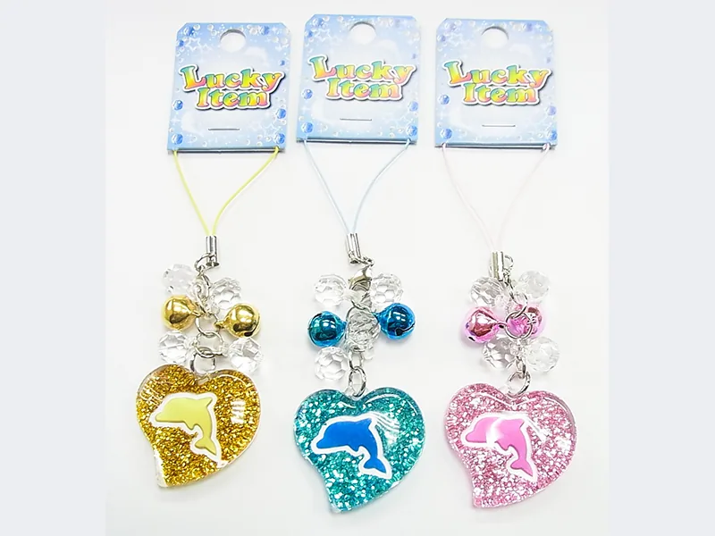 「Lucky Item」の台紙に付いた、イルカの形を抜いたラメ入りのハート形ストラップ3色。金・水色・ピンク。透明な玉と鈴が下がっている