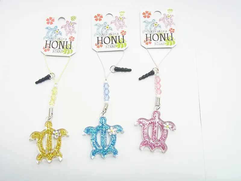「KiraKira HONU」の台紙に付いた、ウミガメ形のラメ入りイヤホンジャック飾り3色。金・水色・ピンク