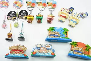 沖縄シリーズの商品を並べた写真。シーサーのキーホルダーとストラップ、「OKINAWA」の台座に乗った置き飾り